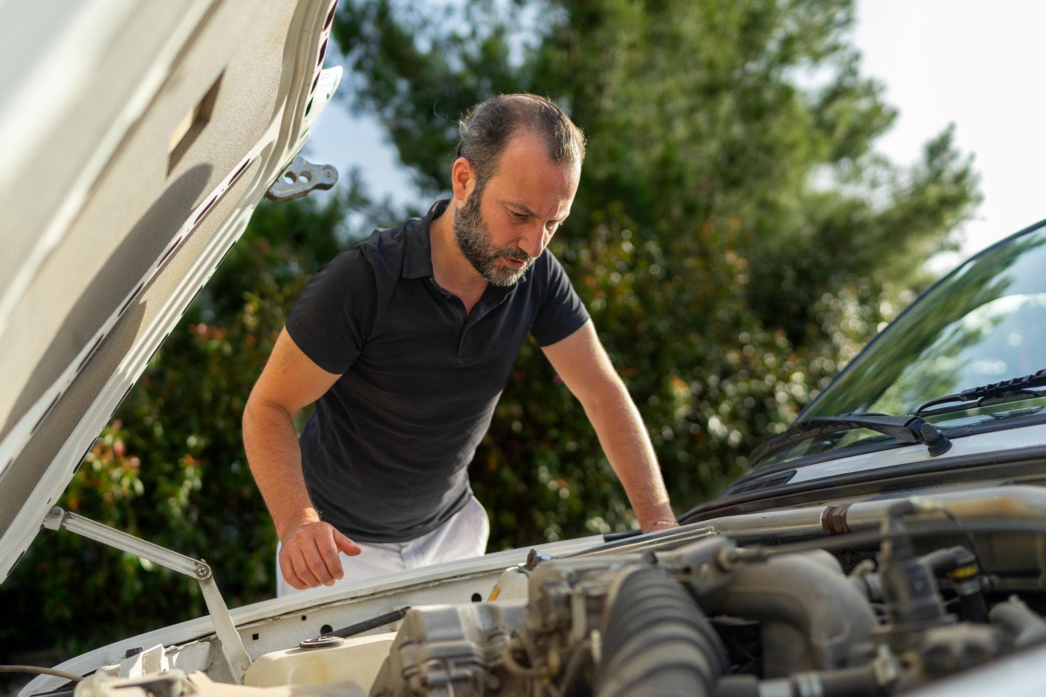 Mand vurderer bilens stand ved åben motorhjelm